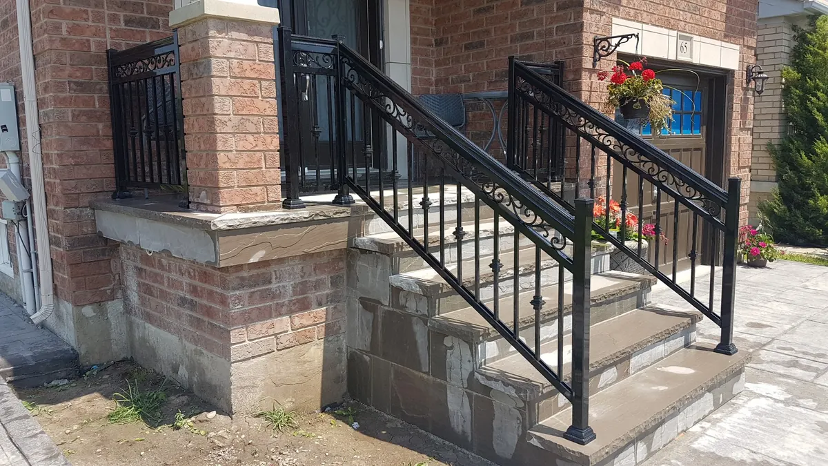 Long black aluminum stair railing with double-post mid-landing on yellow brick