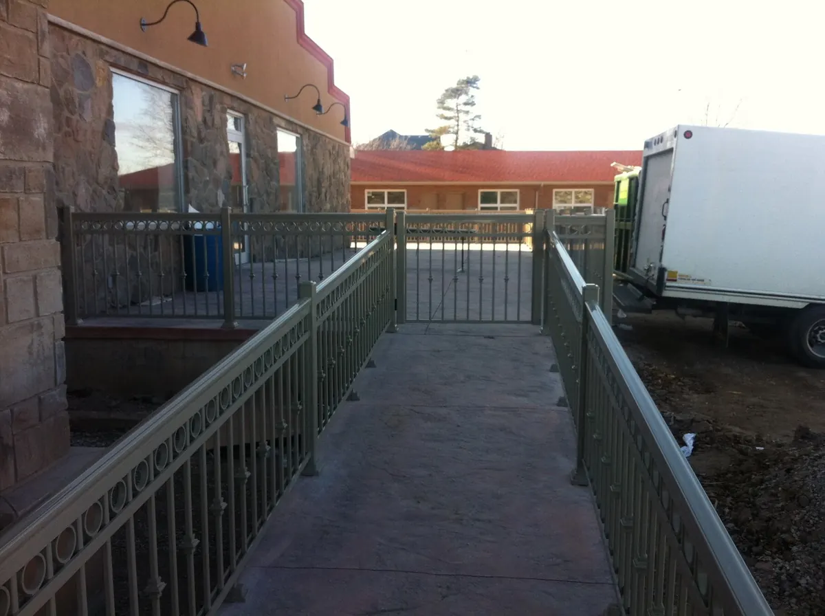 Black aluminum pool fence with self-latch gate along paved walkway