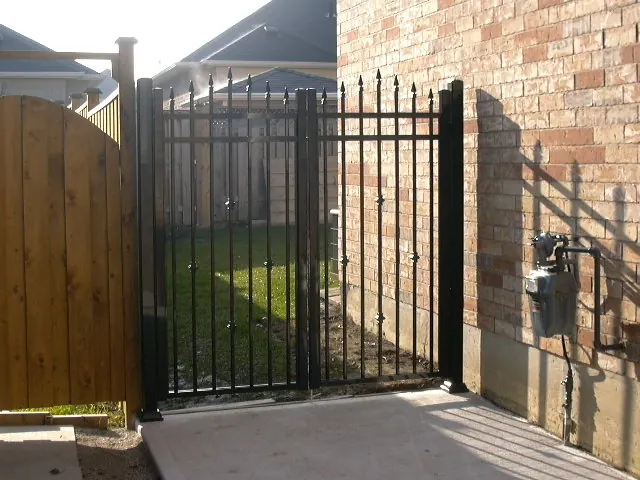 Tall black aluminum spear-top driveway gate next to wood privacy fence